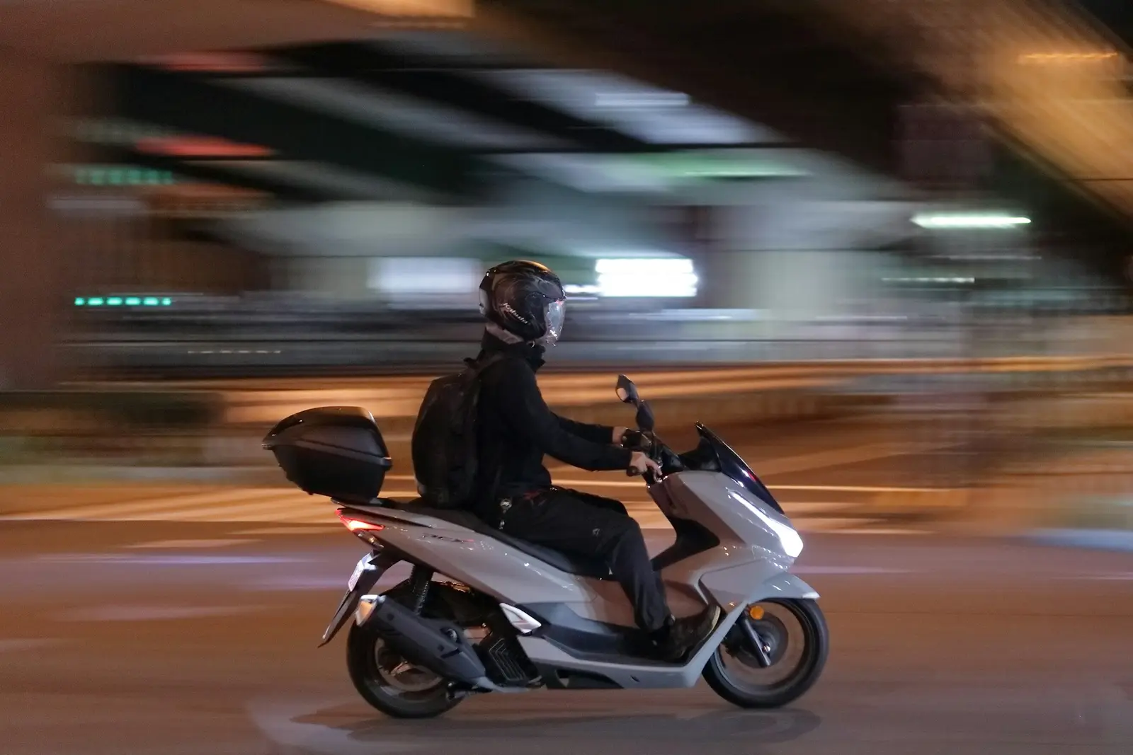שליח עם קסדה על קטנוע ברחוב בלילה, בתנועה